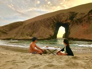 duas pessoas sentadas numa praia com uma mesa na areia em Patitos em Huarmey