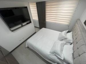 1 dormitorio con 1 cama blanca con almohadas y TV. en Aparta estudio central con ascensor 403, en Bogotá