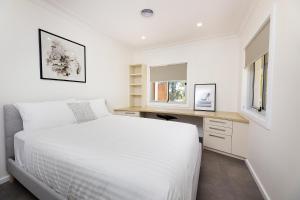 a white bedroom with a bed and a desk at Marine Drive in Forster