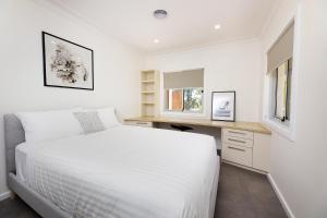 a white bedroom with a bed and a desk at Marine Drive in Forster