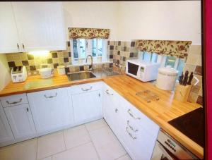 a kitchen with white cabinets and a sink and a microwave at Dove Cot country cottage Ambleside in Ambleside