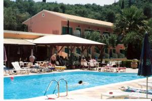 a swimming pool with people sitting in chairs and a building at Camping Paleokastritsa in Paleokastritsa