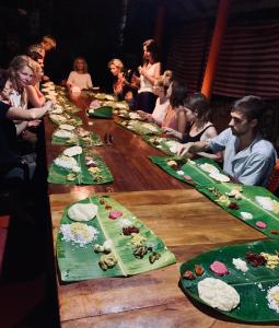 een groep mensen die rond een lange tafel zitten met borden eten bij Green Garden Ayurvedic Resort & Green House in Varkala