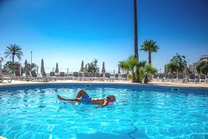 Eine Frau, die auf einem Floß im Schwimmbad liegt. in der Unterkunft Apartamentos Playa Moreia in S'Illot