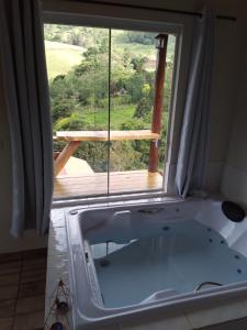 a bath tub in front of a window with a view at Chalé Som do Riacho com Hidromassagem e Lareira á 20 minutos de Gonçalves mg in Gonçalves
