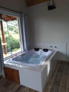 a large white tub in a bathroom with a window at Chalé Som do Riacho com Hidromassagem e Lareira á 20 minutos de Gonçalves mg in Gonçalves