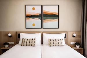 1 Schlafzimmer mit 2 Betten und 2 Gemälden an der Wand in der Unterkunft Strand Suites by NEU Collective in Gżira