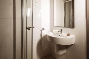 a white bathroom with a sink and a shower at 115 The Strand Hotel by NEU Collective in Il-Gżira