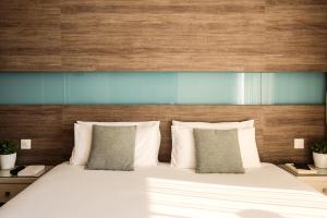 łóżko z białymi poduszkami i drewnianym zagłówkiem w obiekcie 115 The Strand Hotel by NEU Collective w Gżirze