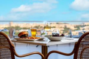 a table with two plates of food and glasses of wine at 115 The Strand Hotel by NEU Collective in Il-Gżira