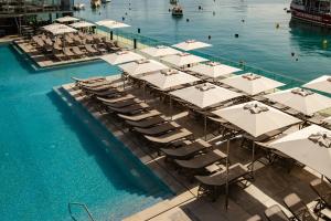 a pool with white umbrellas and chairs in the water at 115 The Strand Hotel by NEU Collective in Il-Gżira