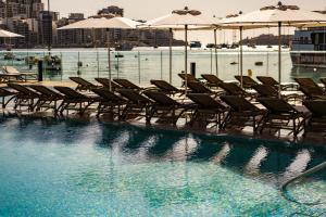 a row of chairs and umbrellas in a swimming pool at 115 The Strand Hotel by NEU Collective in Il-Gżira