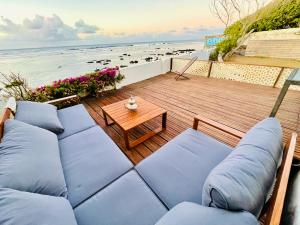 - une terrasse avec des canapés bleus, une table et la plage dans l'établissement Villa Maimouna les pieds dans l'eau, à Saint-Pierre
