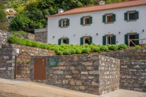 un mur en pierre avec une maison en arrière-plan dans l'établissement Solar dos Reis by An Island Apart, à Ribeira Brava