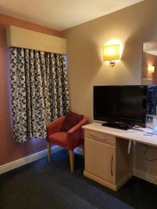 um quarto de hotel com uma secretária, uma televisão e uma cadeira em The Windmill Inn 