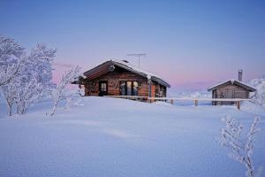 Tunturikelo - beautiful log cottage in the Fells في اتسجوكي: كابينة خشب في الثلج مغطاة بالثلوج