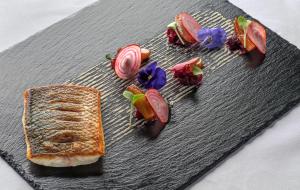 a black plate with food and vegetables on it at The Pelican Beach Resort & SPA - Adults Only in Olbia