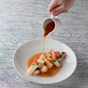 a person pouring sauce onto a plate of food at The Pelican Beach Resort & SPA - Adults Only in Olbia