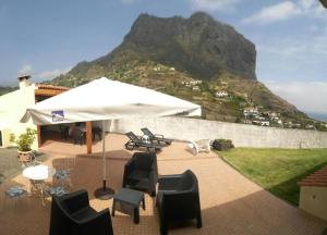 a patio with chairs and an umbrella with a mountain in the background at House pc in Porto da Cruz