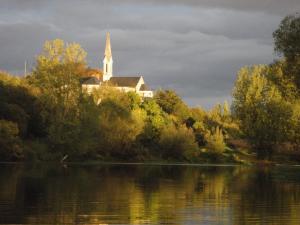 eine Kirche auf einem Hügel neben einem See in der Unterkunft Maison de bourg paisible in Parçay-sur-Vienne