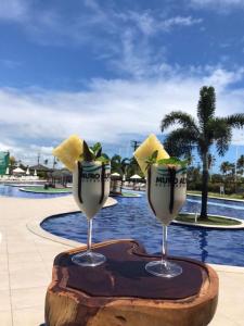 two wine glasses sitting on a table next to a pool at Muro Alto Condomínio Clube Térreo 106 in Porto De Galinhas
