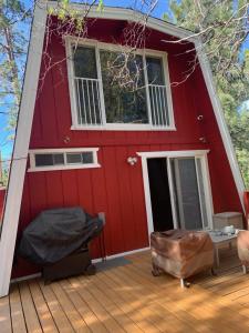 Casa roja con terraza con cama y silla en Maison Solange-Red Barn Farmhouse Style- Moonridge, en Big Bear Lake
