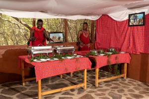 Talek的住宿－Olkinyei Mara Tented Camp，两个人站在帐篷里,餐桌上摆着食物