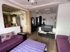 a living room with a purple couch and a tv at Cité Jardins Appartement in Martil