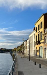 a sidewalk next to a river with buildings next to the water at Appartement spacieux & calme avec vue sur l'Escaut in Tournai