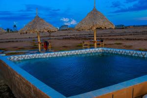 una piscina con due ombrelloni di paglia e una spiaggia di Amanya Camp 1-Bed Tent Elephant Suite in Amboseli ad Amboseli