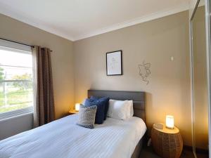 Stunning Hobart 3-bed home- close to shopping centers في Glenorchy: غرفة نوم بسرير ومصباح ونافذة