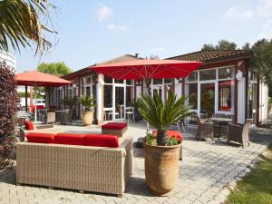 un patio con sillas, mesas y una sombrilla en Kyriad Nîmes Ouest A9 en Nimes