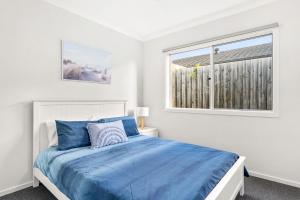 a white bedroom with a blue bed and a window at The Seas at Phillip Island in Cowes