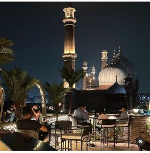 grupa ludzi siedzących w nocy przy stolikach na dachu w obiekcie Hotel Aiwan-e-Shahi w Nowym Delhi