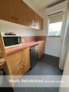 a kitchen with wooden cabinets and a microwave at Summerhill Motor Inn in Merimbula
