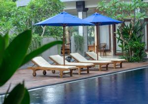 a group of chairs and umbrellas next to a pool at Gria Manik Batubelig in Seminyak