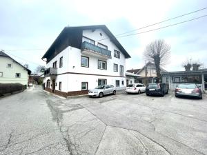 a white house with cars parked in a parking lot at Pension Maier in Villach