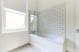 een witte badkamer met een bad en een raam bij The Fulham Escape - Alluring 5BDR Flat in Londen