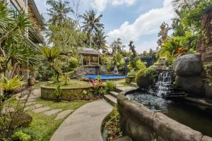a garden with a waterfall and a swimming pool at Gynandha Ubud Cottage in Ubud