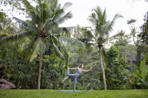 a woman doing yoga in front of two palm trees at The Allure Ubud Villas & Spa crafted by freshWater Asia in Ubud