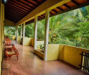 a porch of a house with chairs and palm trees at Blue Magpie Lodge Sinharaja in Kudawe