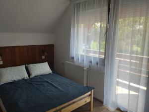 a bedroom with a bed with a blue blanket and a window at Börzsöny Vendégház in Zebegény