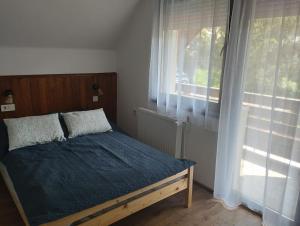 Schlafzimmer mit einem Bett mit blauer Bettwäsche und einem Fenster in der Unterkunft Börzsöny Vendégház in Zebegény