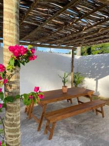 einen Holztisch und eine Bank unter einem Dach mit Blumen in der Unterkunft Casa Palma in São Miguel do Gostoso