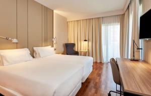 Habitación de hotel con cama blanca grande y escritorio. en NH Luz Huelva, en Huelva