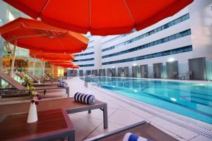 um hotel com piscina e guarda-sóis e cadeiras vermelhas em Holiday Villa Hotel & Residence City Centre Doha em Doha