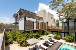 a building with a swimming pool and some chairs and umbrellas at Lumina at Mudra Tulum in Tulum