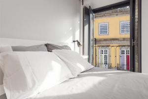 una cama con sábanas blancas y una ventana con un edificio en Be In Oporto, en Oporto