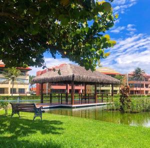 um banco de parque em frente a um pavilhão com telhado de relva em Ap Aquaville resort -CE em Aquiraz