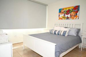 Un dormitorio con una cama blanca y una pintura en la pared en Apartamento frente a la Playa Arecibo Puerto Rico, en Arecibo